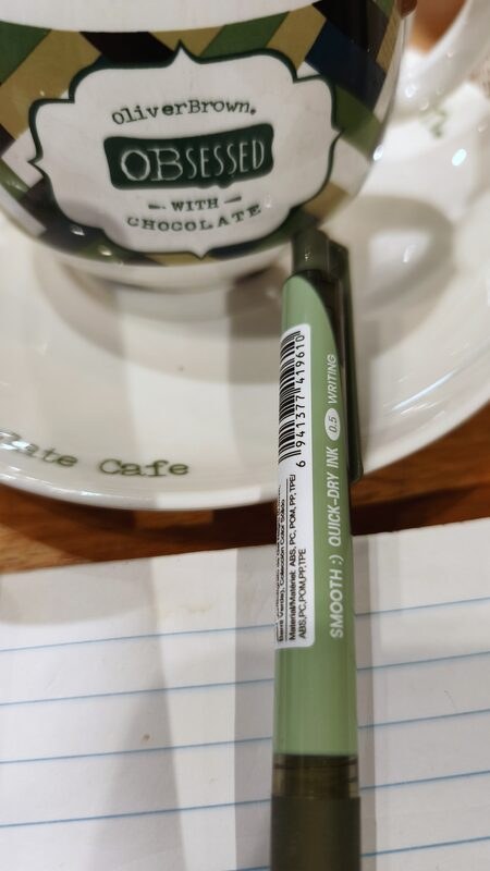 My own photo from that Sunday: a mug on a saucer, a green pen and a lined notepad on the café table