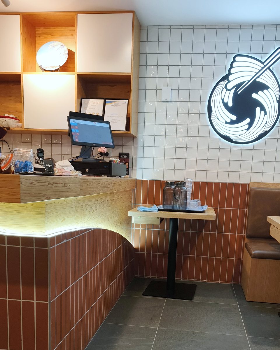 Inside Kajiken Brisbane: counter, white tiled wall with the Kajiken noodle-bowl logo, and booth seating